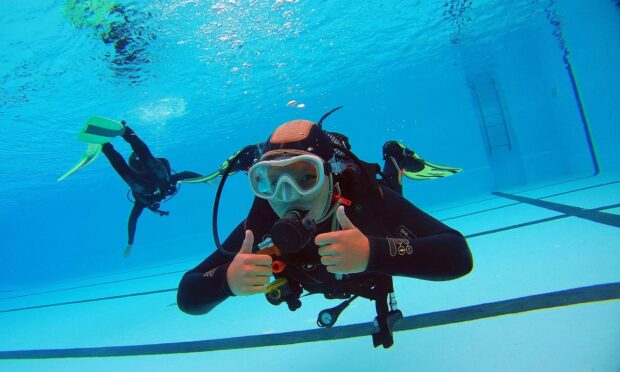 A scuba diver giving thumbs up underwater in a pool during a scuba diving training session