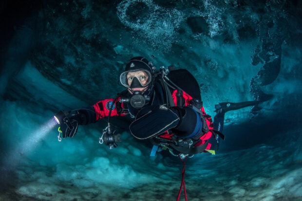 A scuba diver exploring an underwater cave with a flashlight in full gear