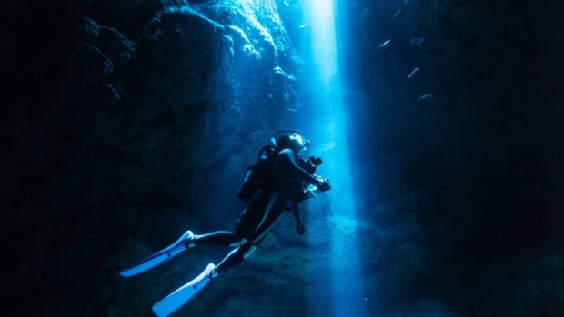 Scuba diver exploring underwater caves with natural light beams