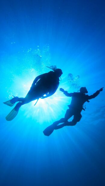 Two scuba divers exploring underwater in deep blue ocean with sunlight rays