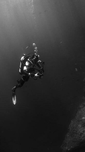 A scuba diver exploring underwater near a rocky cliff in deep ocean