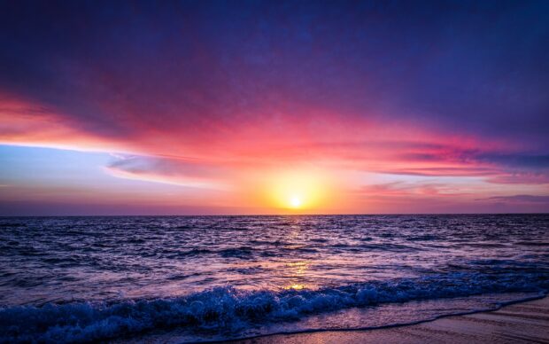 Vibrant seascape with a colorful sunset over the ocean horizon and waves gently crashing on the shore