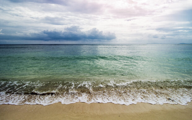Calm waves gently touching the sandy shore under cloudy skies in seascape