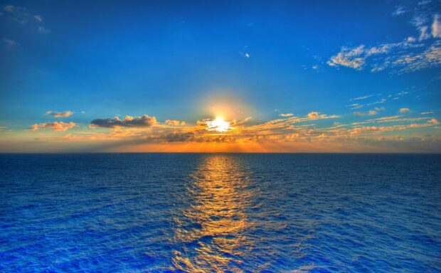 Sun setting over the ocean horizon with dramatic sky and calm sea waves