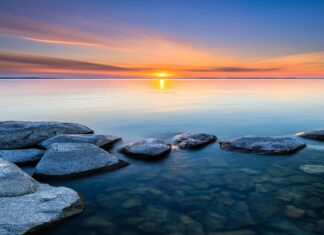 Calm seascape with rocks in clear water and sunrise on the horizon