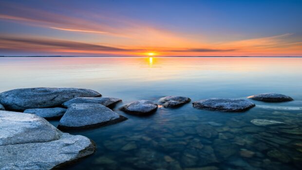 Calm seascape with rocks in clear water and sunrise on the horizon