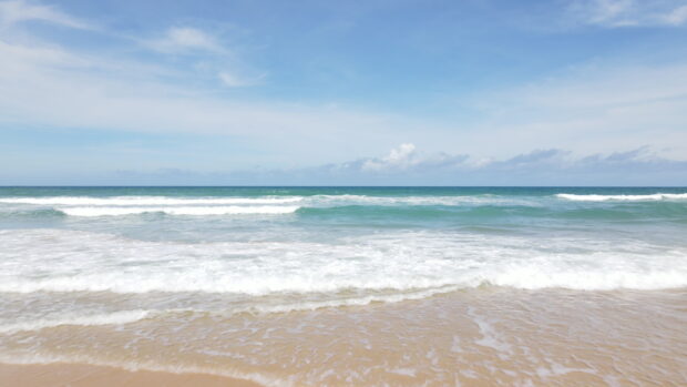 Calm seascape with waves gently rolling onto a sandy shore under a clear blue sky