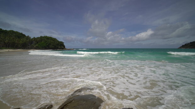 Calm turquoise seascape with gentle waves and lush green coastline under cloudy sky