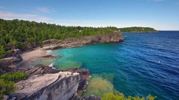 Clear turquoise seascape with rocky cliffs and lush green forest in the background