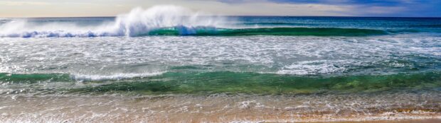 Crystal clear seascape with waves crashing on a sandy shore under a blue sky