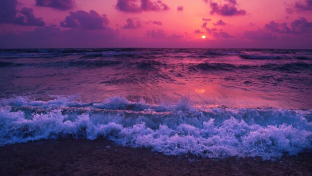 Purple sunset over seascape with waves crashing on the shore