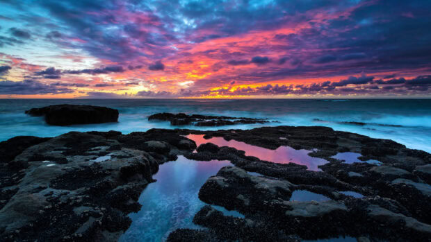 Rocky coast with tidal pools reflecting colorful sunset sky over the seascape horizon