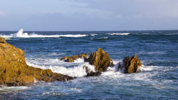Waves crashing against rocky seascape with deep blue ocean and clear sky