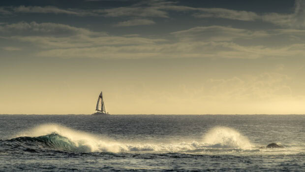 A sailboat sailing on the sea with waves crashing under a cloudy sky