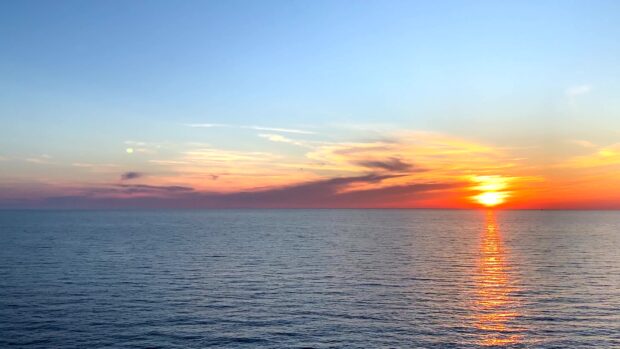 A serene seascape with a vibrant sunset over calm ocean waters and colorful sky clouds
