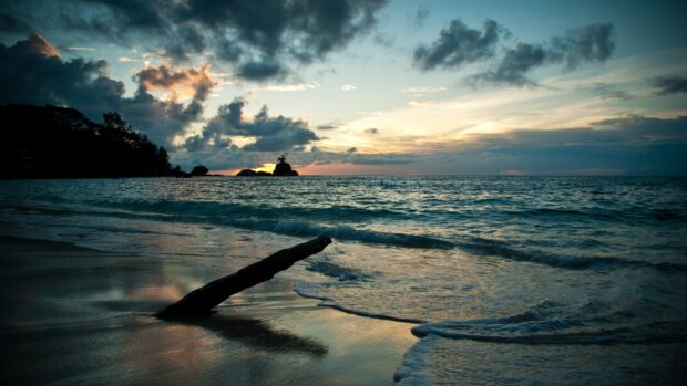 A serene seascape with waves gently crashing on the shore and a dramatic cloudy sky at sunset