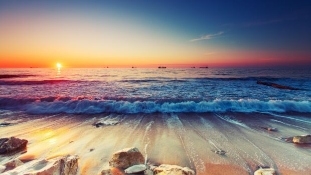 Calm ocean waves approaching rocky shore during vibrant sunset seascape