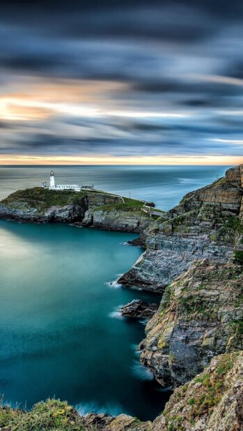 A peaceful seascape with cliffs and a lighthouse under a cloudy sky