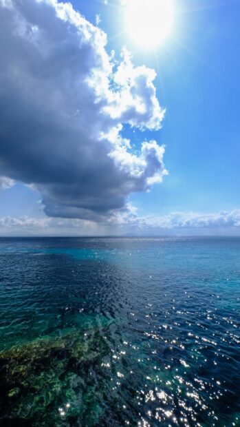 Clear blue seascape with sunlight sparkling on water and large clouds above the horizon