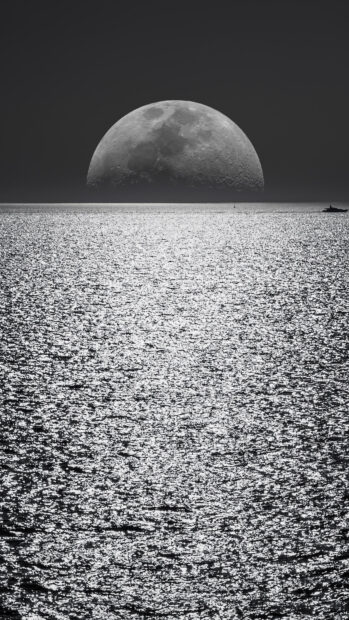The moon rises over the shimmering seascape reflecting light on the water surface