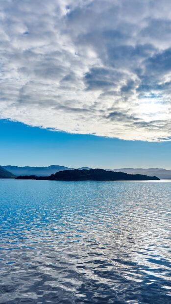 Calm seascape with an island under a cloudy sky reflecting on the water