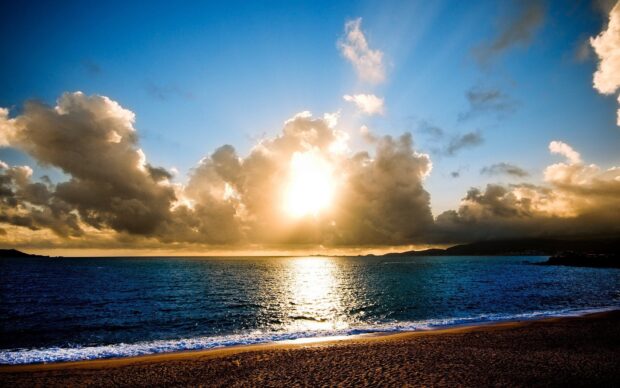 A serene seascape with dramatic clouds and sun reflecting over the calm ocean waters