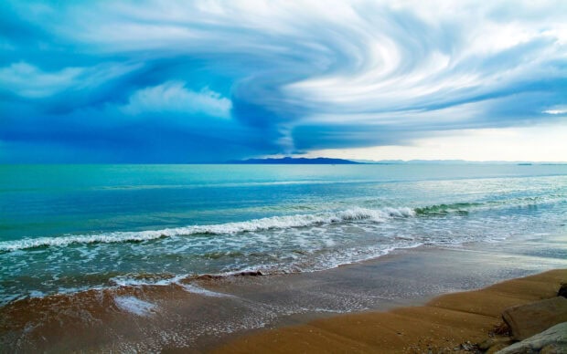 Calm seascape with swirling clouds over the ocean and sandy beach under dramatic sky