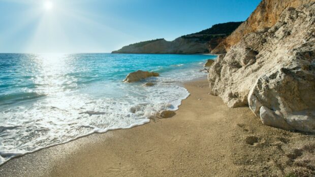 Rocky coastline with turquoise sea waves under bright sun on a sandy beach