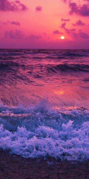 Purple sunset seascape with waves crashing on shore at twilight