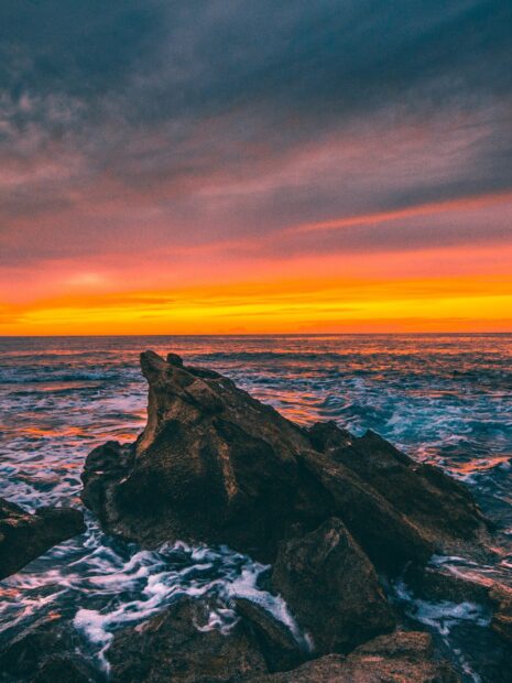Rocky seascape at sunset with colorful sky and ocean waves crashing