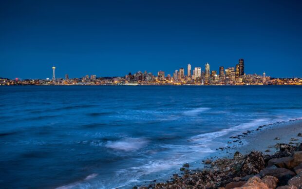Night view of Seattle city skyline with water and rocky shore in the foreground