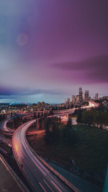 Curved highway leading to Seattle cityscape at dusk with vibrant lights and purple sky