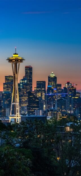 Seattle skyline featuring the Space Needle at dusk with city lights and trees in the foreground