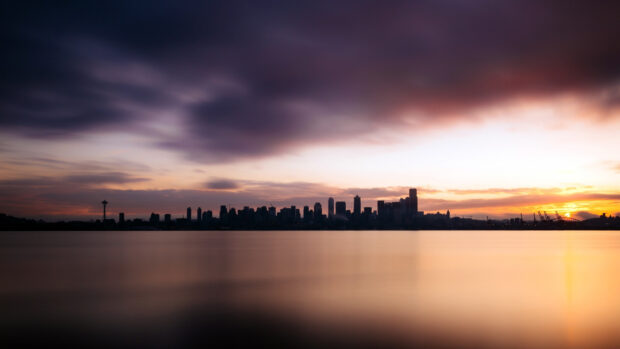 Seattle skyline silhouette at sunset with calm water and cloudy sky in the background