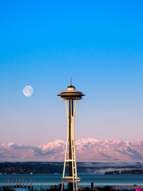 The Seattle skyline featuring the space needle with snowy mountains and the moon in the background