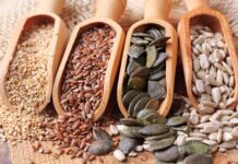 Four kinds of seeds displayed in wooden scoops on a rustic surface