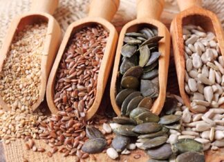 Four kinds of seeds displayed in wooden scoops on a rustic surface