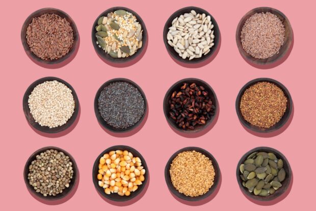 A variety of seeds arranged in wooden bowls on a pink surface displaying different types of seeds