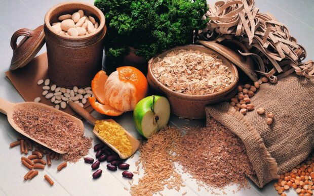 A variety of seeds displayed alongside an apple and peeled orange on a table
