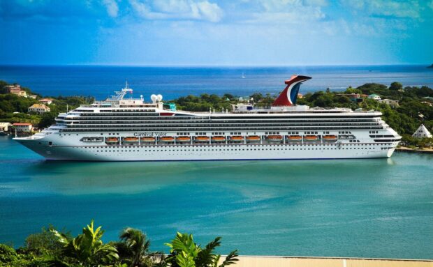 A large ship docked near a tropical island with clear blue water and green foliage