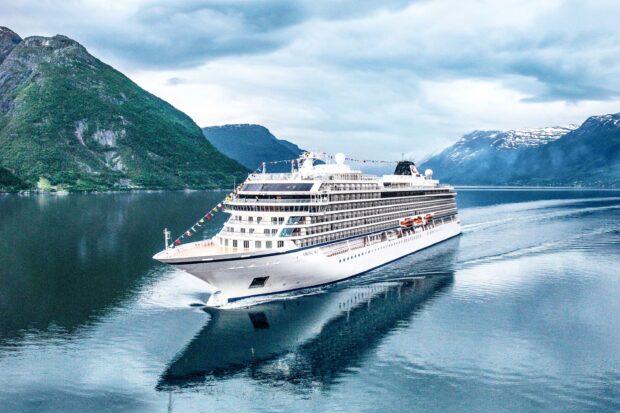 Large ship cruising through calm fjord waters surrounded by mountainous terrain