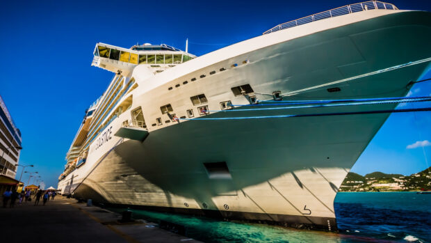 Large cruise ship docked at port under clear blue sky with vibrant water