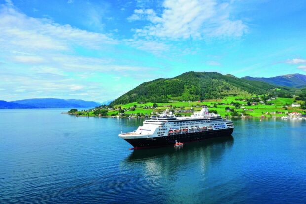 A cruise ship sailing near a green hillside along the coastline under a blue sky