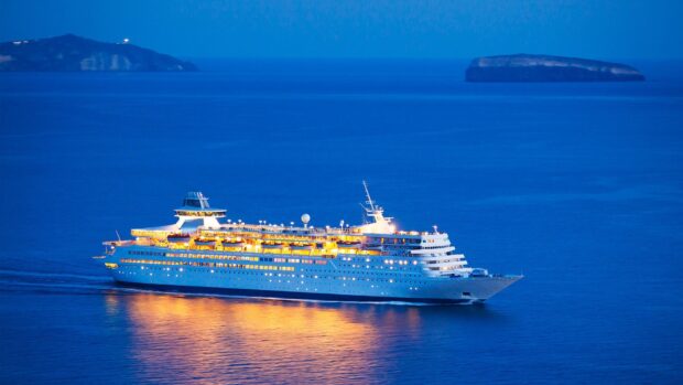 A large ship sailing on calm blue water during twilight with illuminated decks
