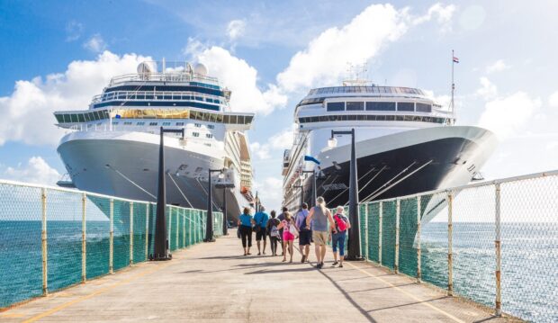 People walking on pier between large ship vessels under blue sky