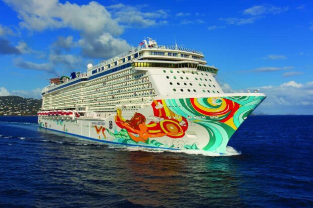 A cruise ship with colorful artwork sailing on clear blue ocean under a partly cloudy sky