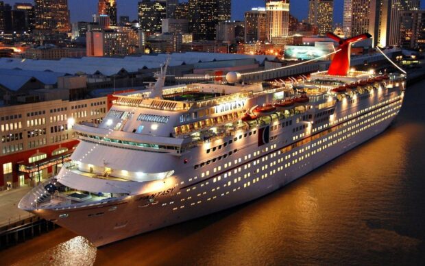 A large cruise ship docked at the port during nighttime with city lights in the background