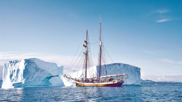 A classic ship sailing near large icebergs in calm blue waters with clear skies