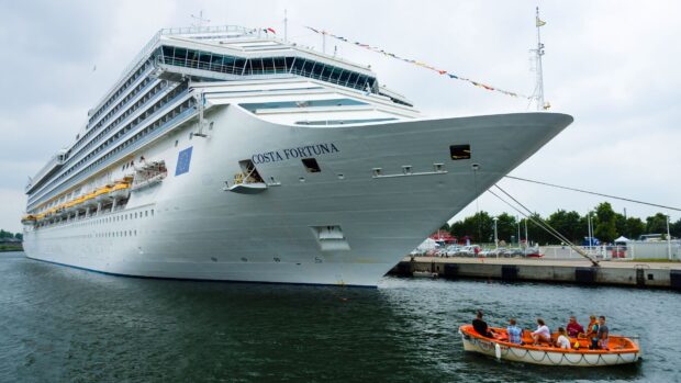 A large ship docked at the harbor with people on a smaller boat nearby