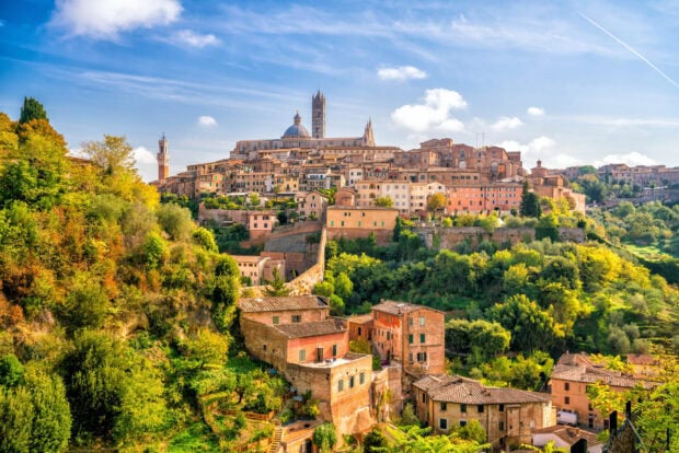 Historic Siena cityscape surrounded by lush greenery and vibrant autumn trees in Tuscany Italy